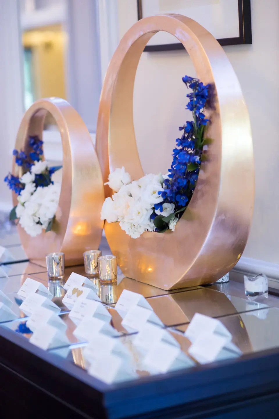 Gold rings filled with white flowers and blue delphinium above the escort cards.