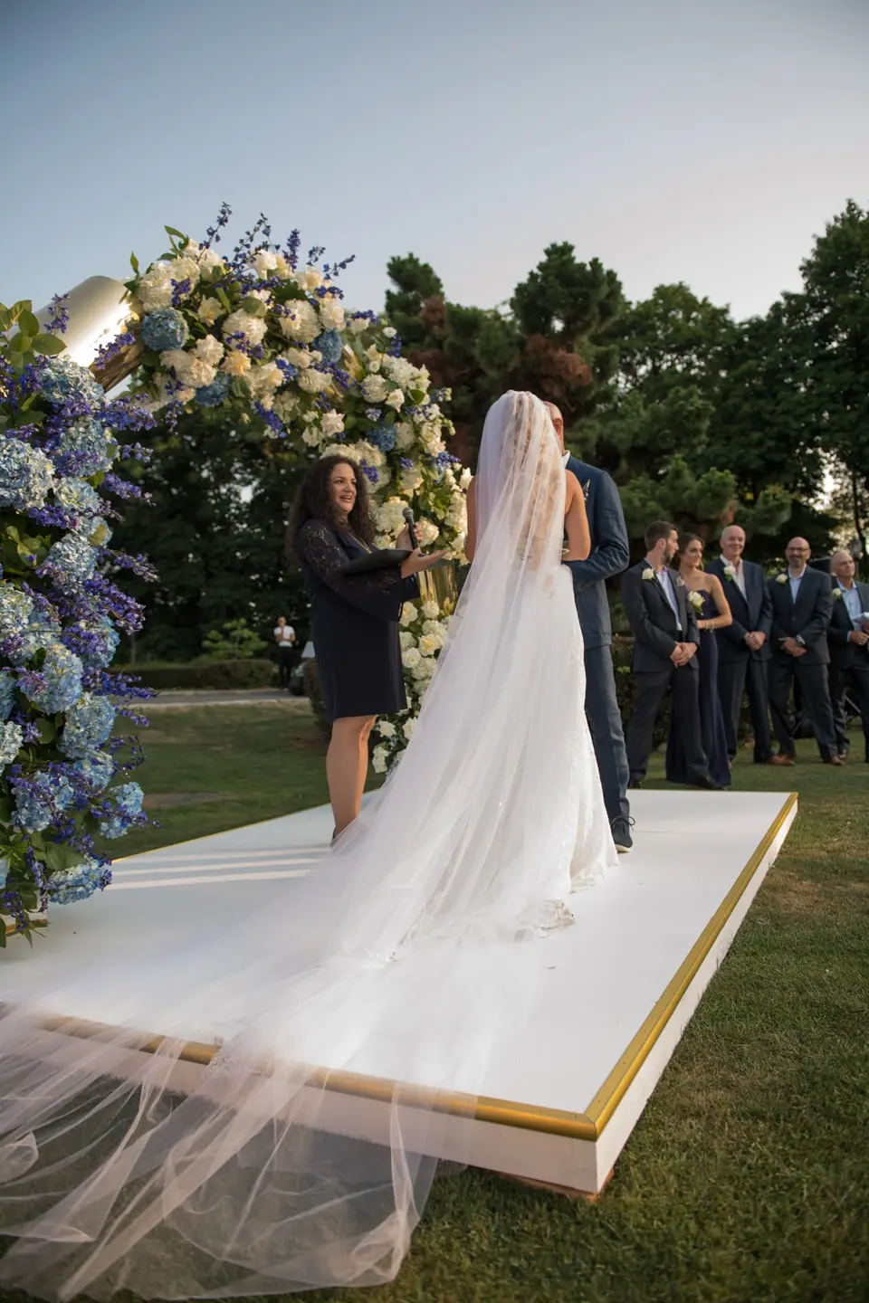 Seen from behind, the bride's veil spreads across the white platform beneath the arch.
