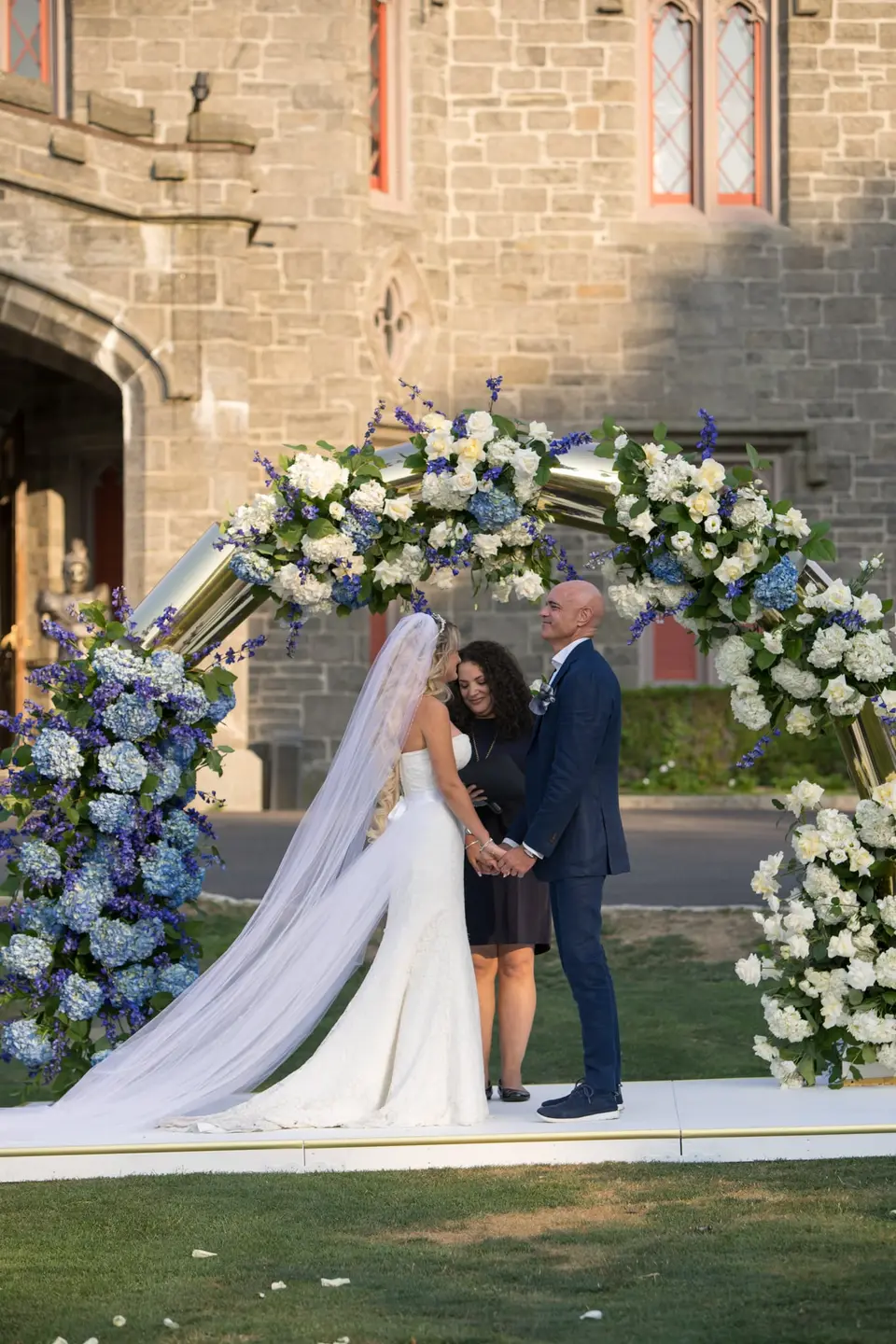 The bride and groom hold hands beneath the arch before the castle doorway.