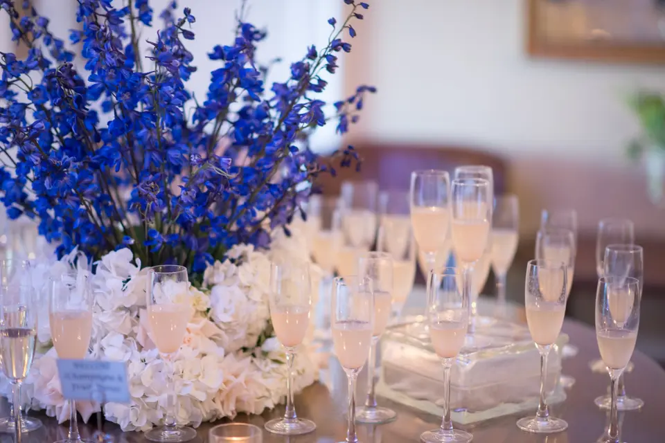 Glasses of champagne beside a low arrangement of white hydrangeas and blue delphinium.