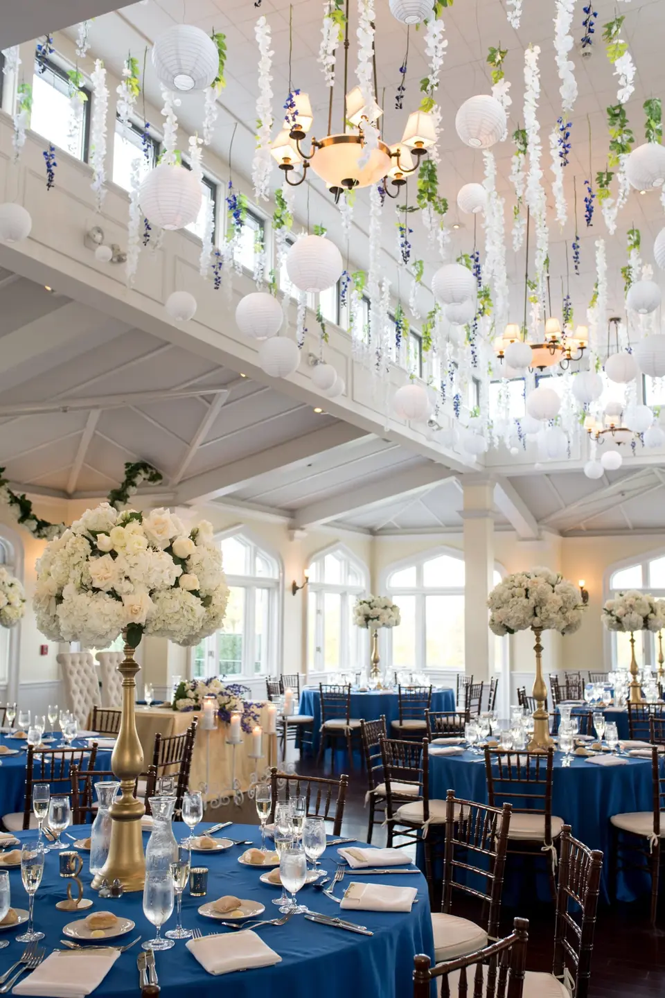 The reception room beneath hanging paper lanterns and white wisteria, tables in deep blue linen.