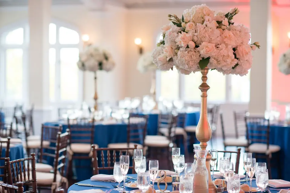 A tall arrangement of blush roses on a gold stand above a table in blue linen.