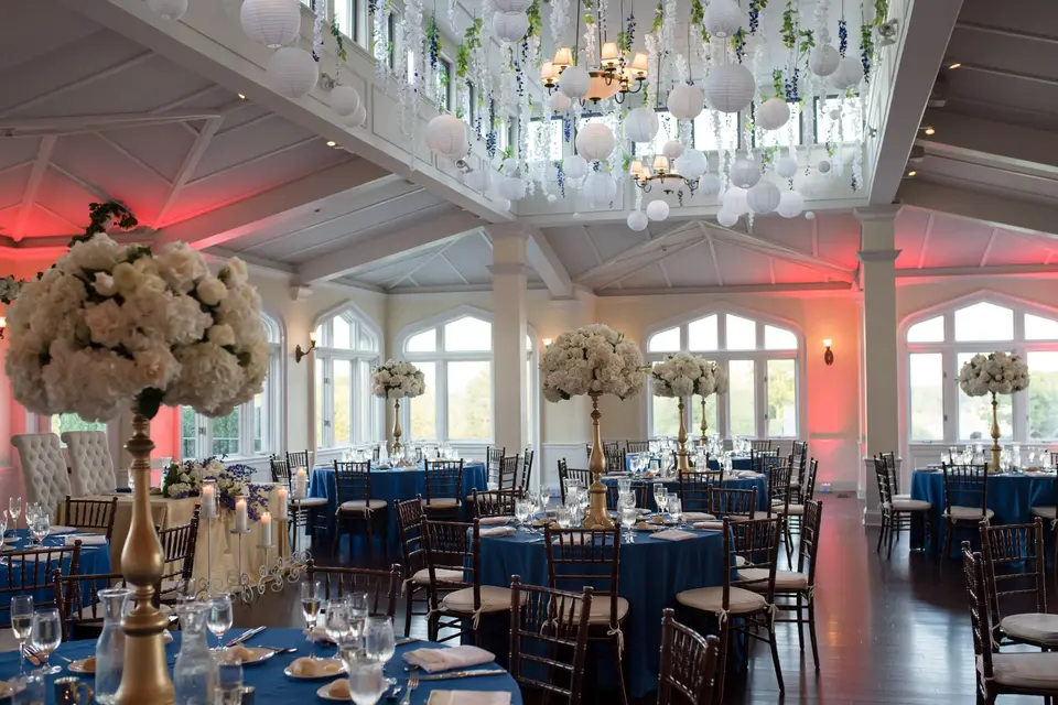 The reception room set for dinner, tall white and blush arrangements above tables in deep blue.