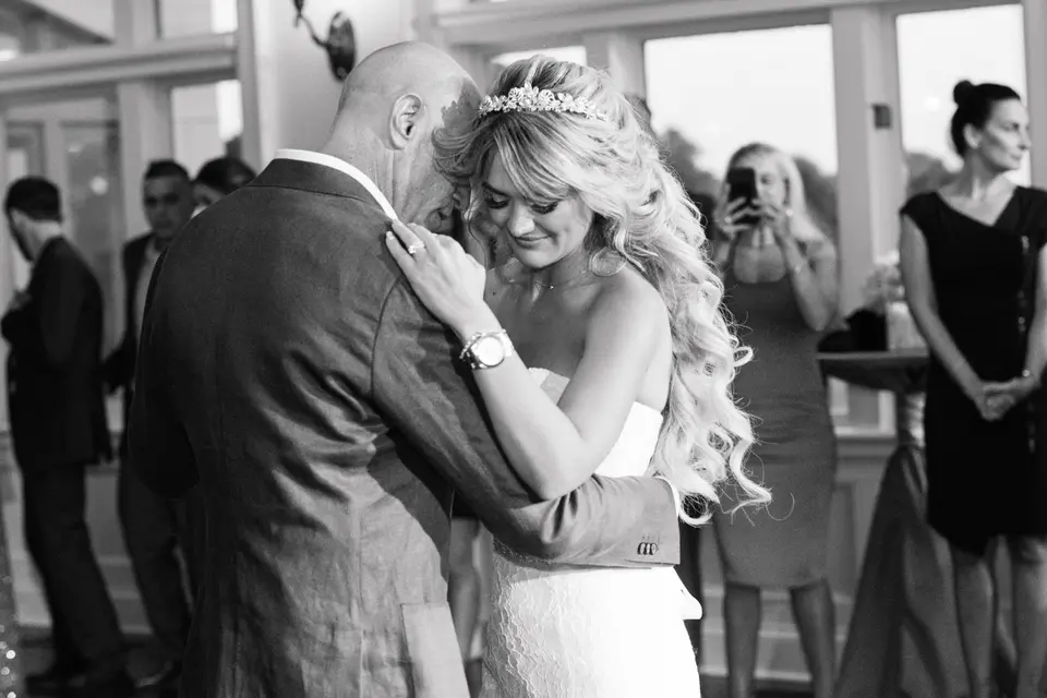 The bride and groom share their first dance, guests watching. Black and white.