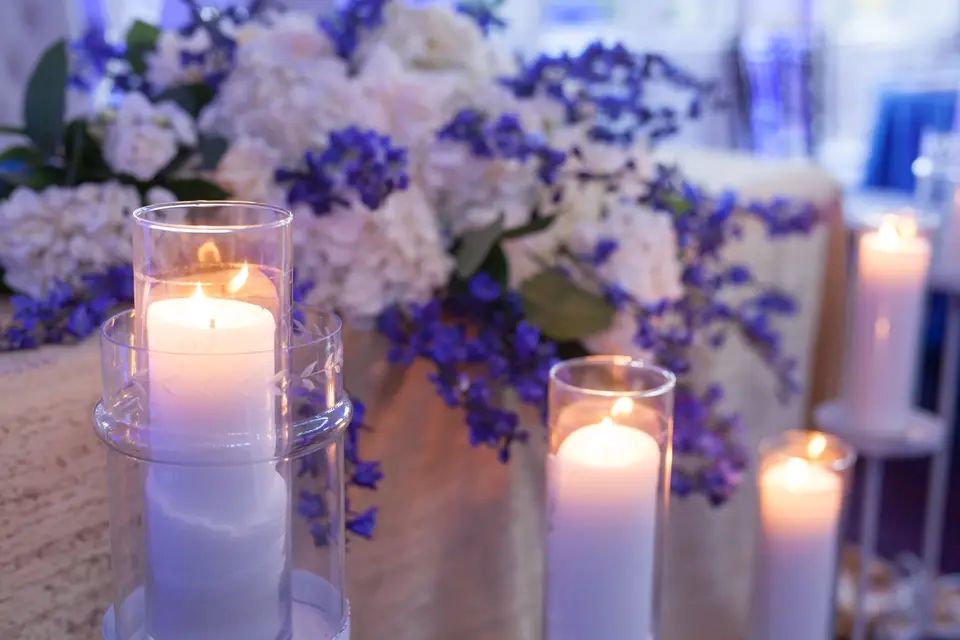 Pillar candles in glass holders among white hydrangeas and blue delphinium.