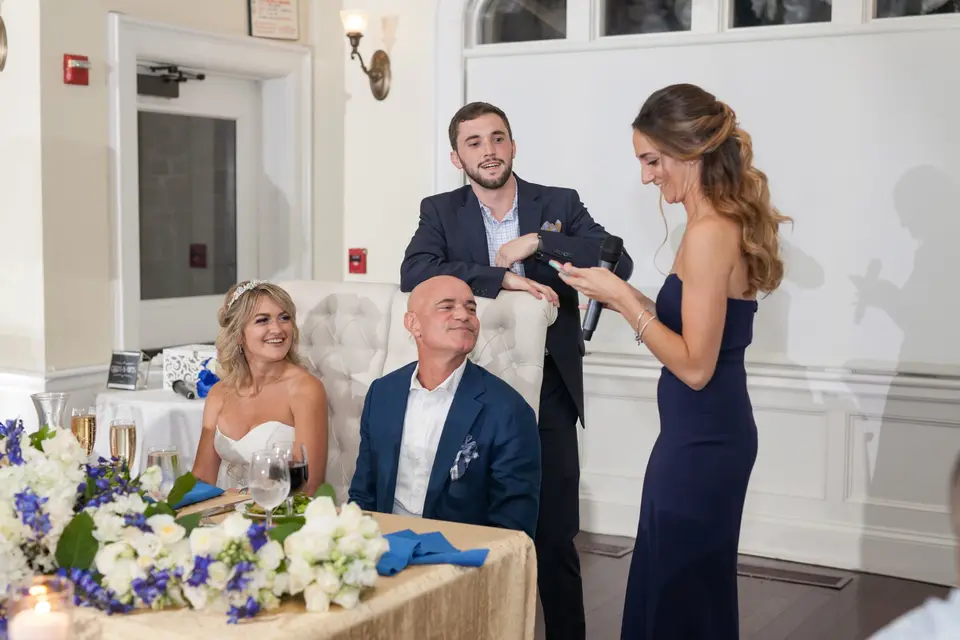 The bride and groom listen at their table as a guest gives a toast.