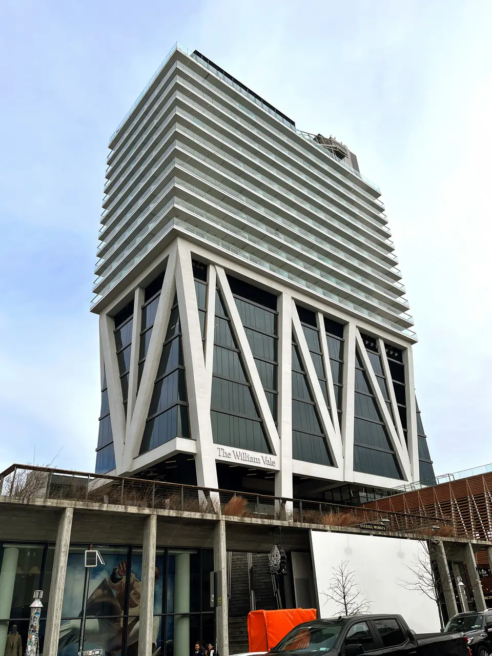 The William Vale in Williamsburg, a white tower raised on angled concrete legs above a public park, against a bright sky.