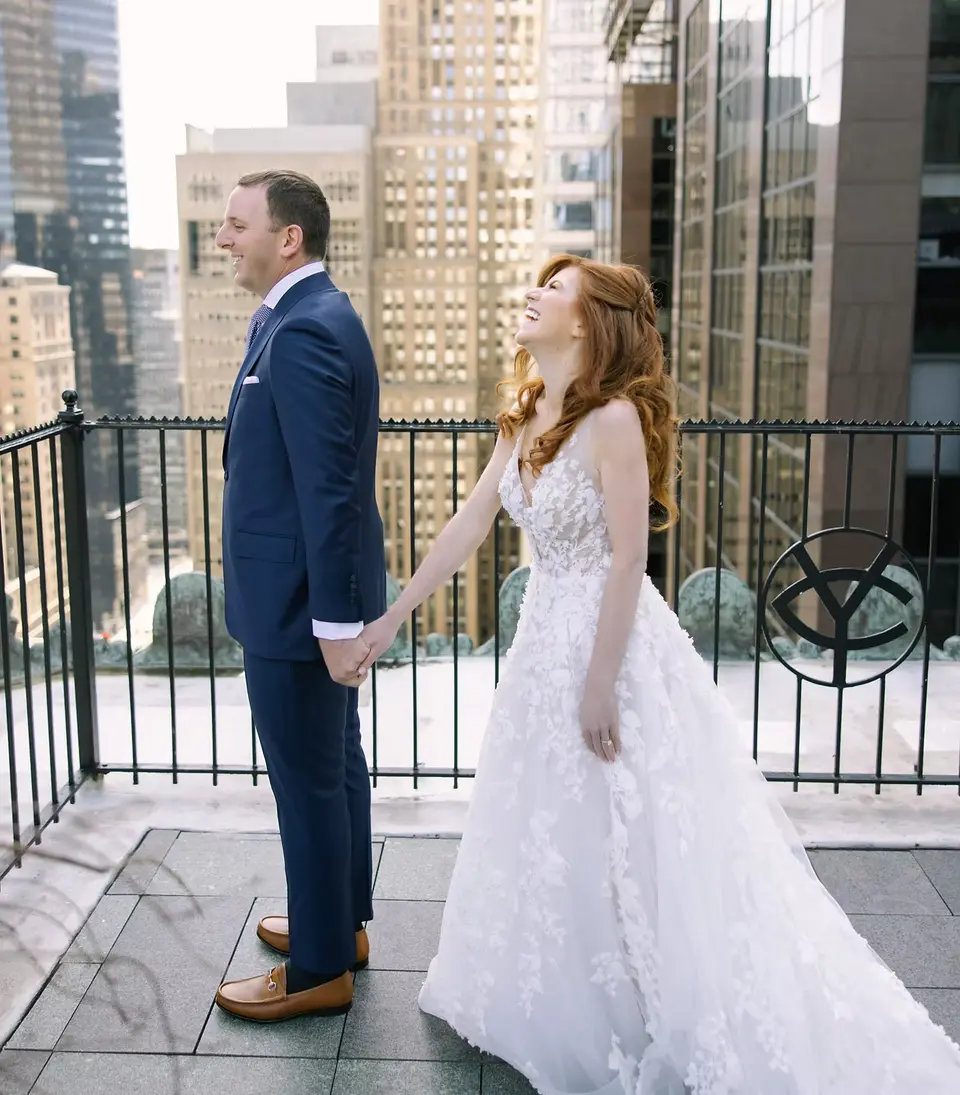 On the roof terrace of the Yale Club, the groom holds his bride's hand as she laughs, the towers of Midtown behind them.