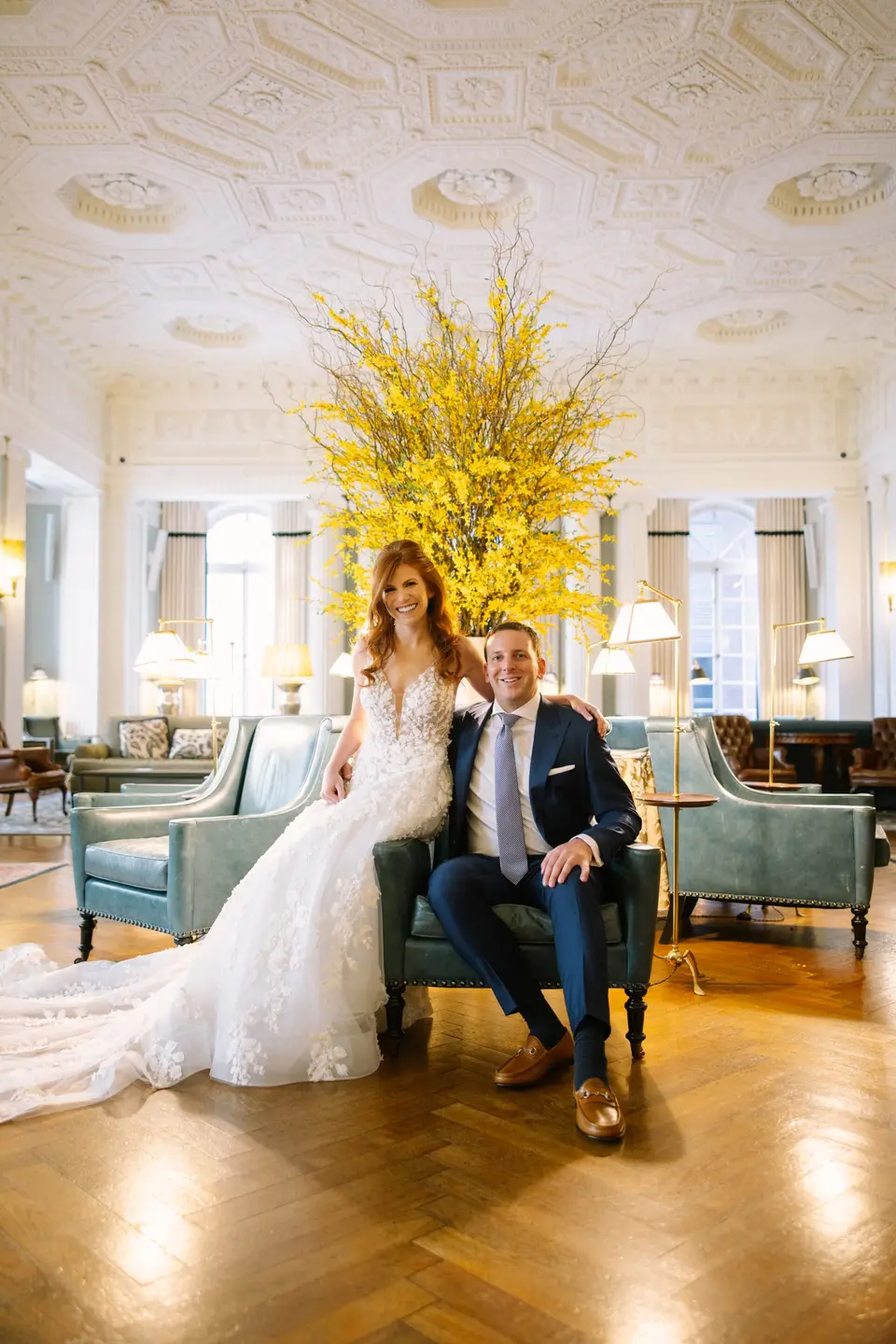 The bride and groom sit in a leather armchair in the club's lounge beneath a great arrangement of yellow forsythia.