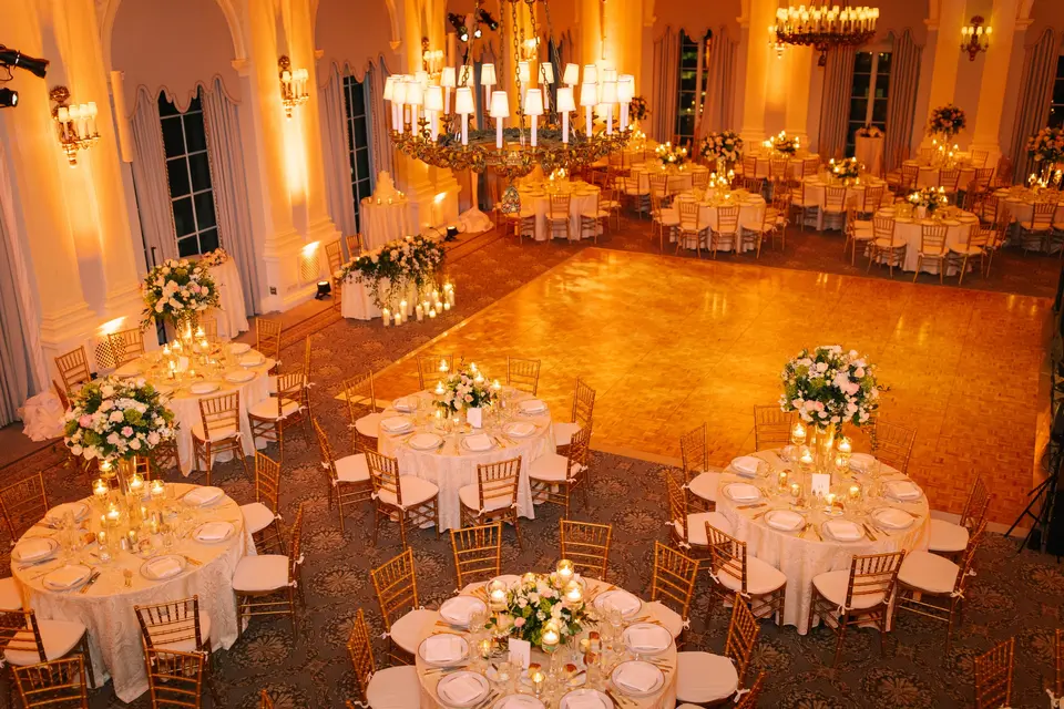 The ballroom seen from above in warm light, round tables with white arrangements around the dance floor.