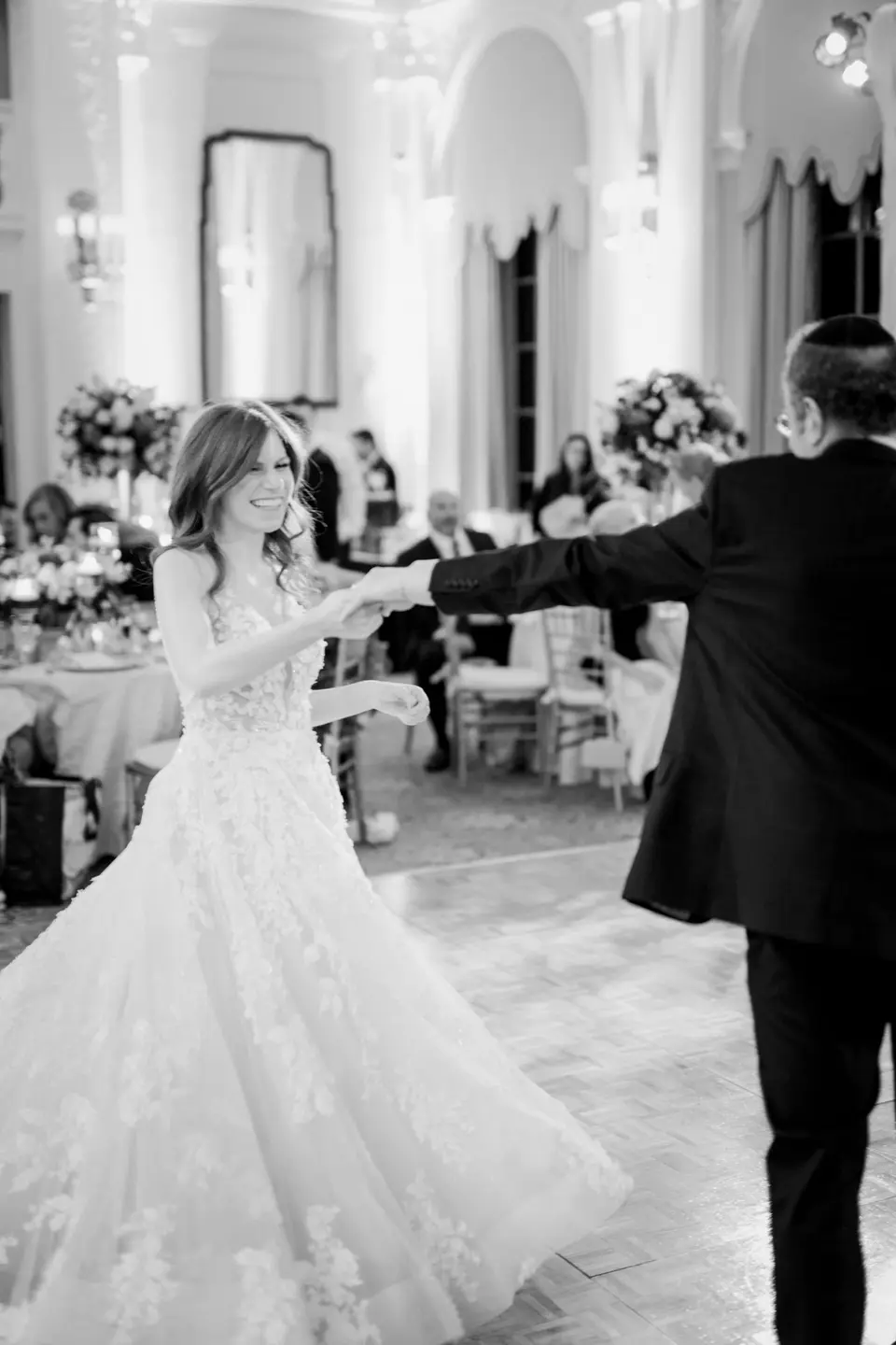The bride dances with her father, her gown swirling. Black and white.