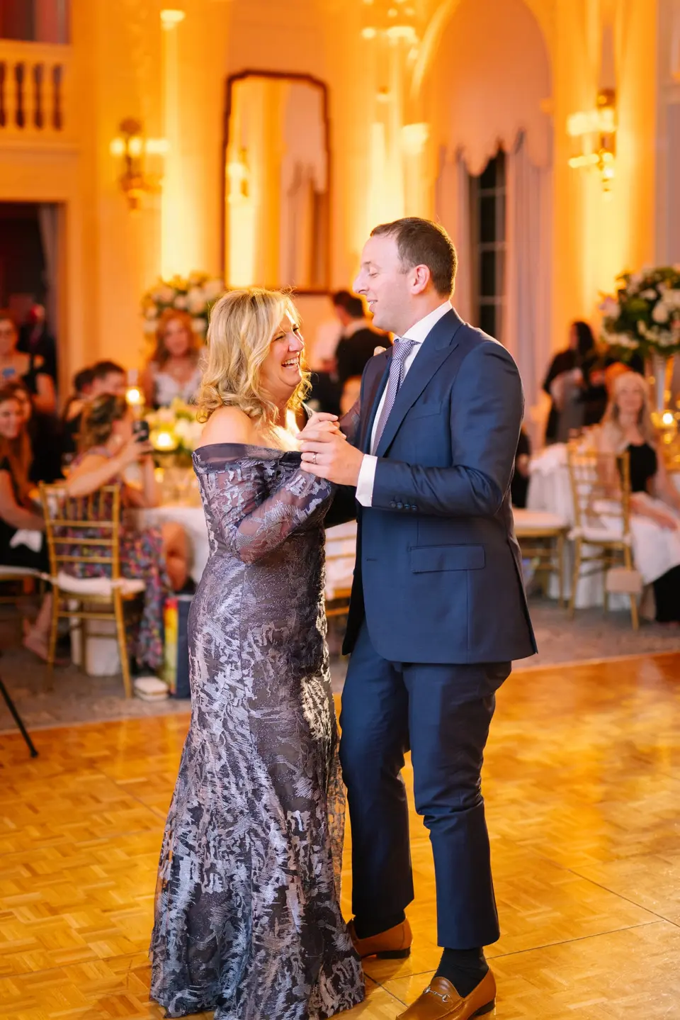 The groom dances with his mother in the warm light of the ballroom.