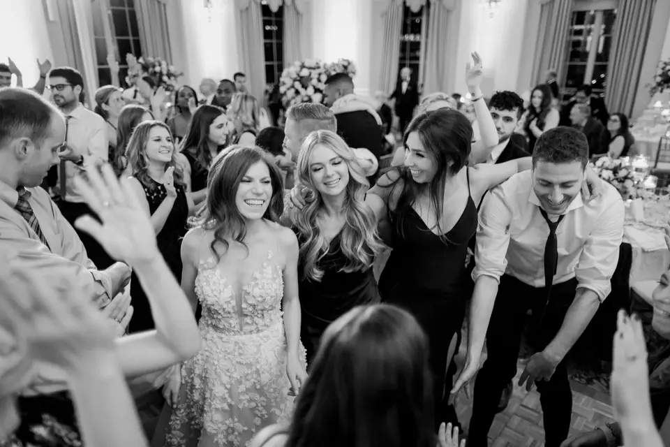 The bride dances among friends with their hands in the air. Black and white.